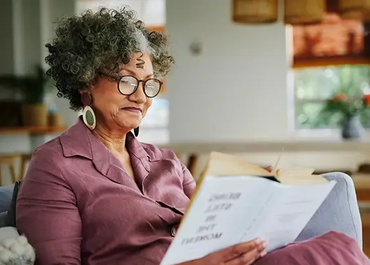Une femme senior avec des lunettes lit un livre.